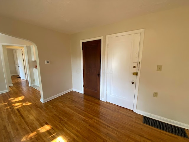 unfurnished bedroom with baseboards, visible vents, arched walkways, and wood finished floors