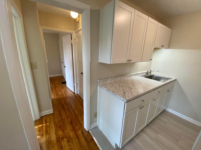 kitchen featuring a sink, white cabinetry, baseboards, light wood-style floors, and light countertops