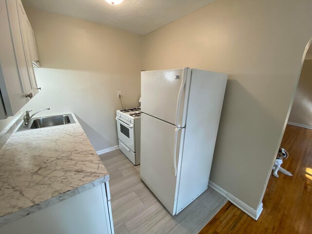 kitchen with white appliances, a sink, white cabinetry, baseboards, and light countertops