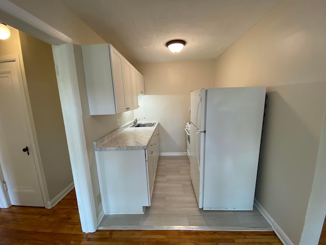 kitchen with light countertops, freestanding refrigerator, white cabinetry, a sink, and baseboards