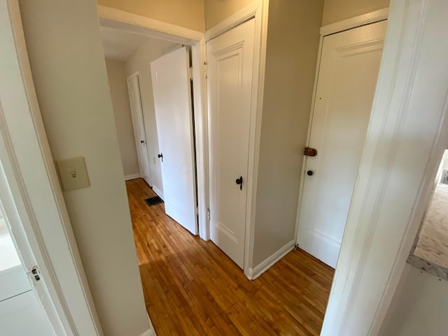 hall featuring visible vents, baseboards, and hardwood / wood-style flooring