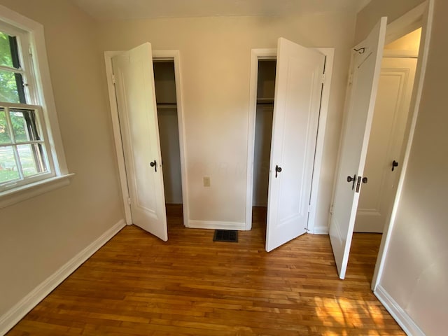 unfurnished bedroom with visible vents, two closets, baseboards, and wood finished floors