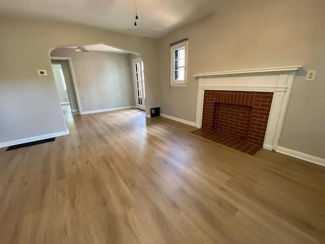 unfurnished living room featuring arched walkways, a brick fireplace, wood finished floors, and baseboards