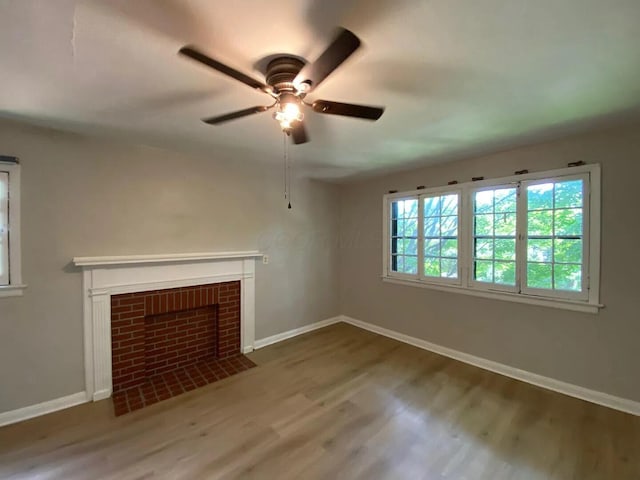 unfurnished living room featuring a brick fireplace, ceiling fan, baseboards, and wood finished floors