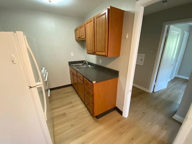 kitchen with dark countertops, light wood-style flooring, brown cabinetry, freestanding refrigerator, and a sink