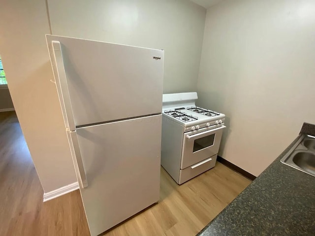 kitchen with white appliances, baseboards, dark countertops, light wood-type flooring, and a sink