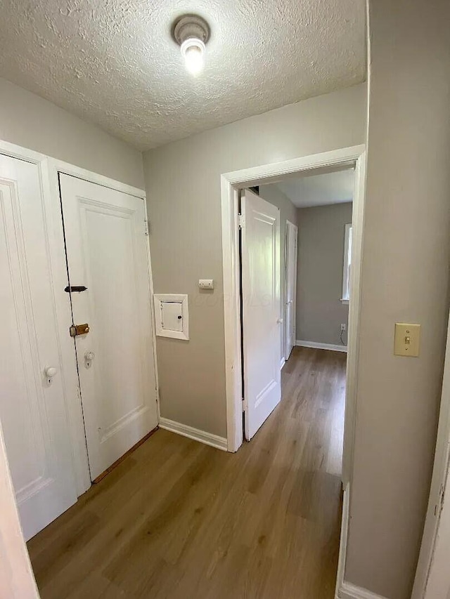 hallway with a textured ceiling, baseboards, and wood finished floors