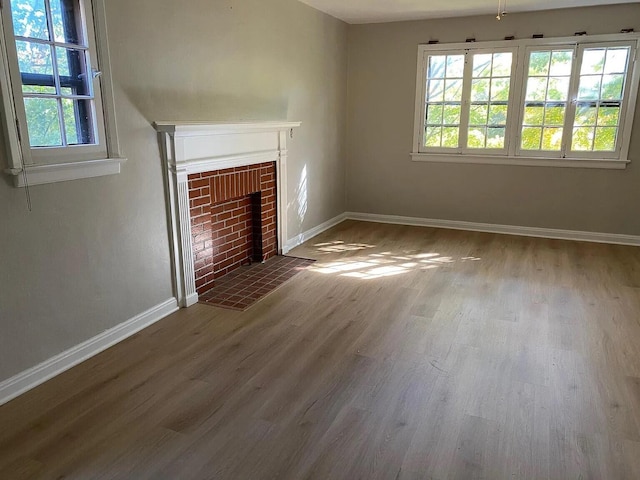 unfurnished living room featuring a brick fireplace, baseboards, and wood finished floors