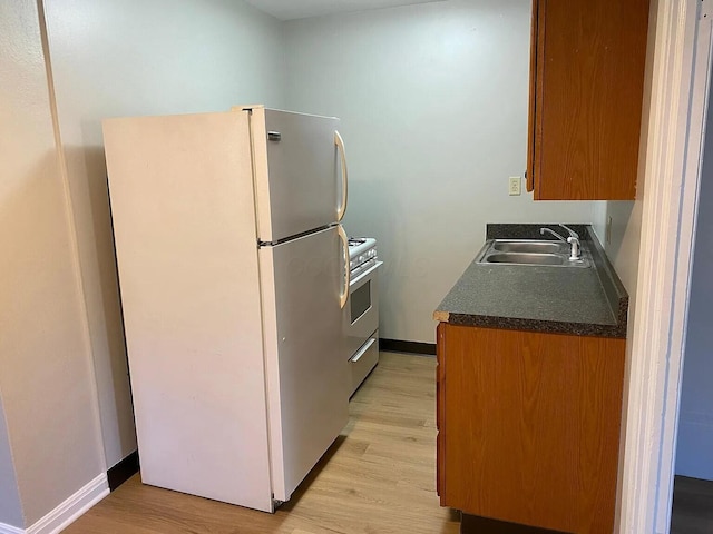 kitchen with freestanding refrigerator, a sink, light wood finished floors, and gas range