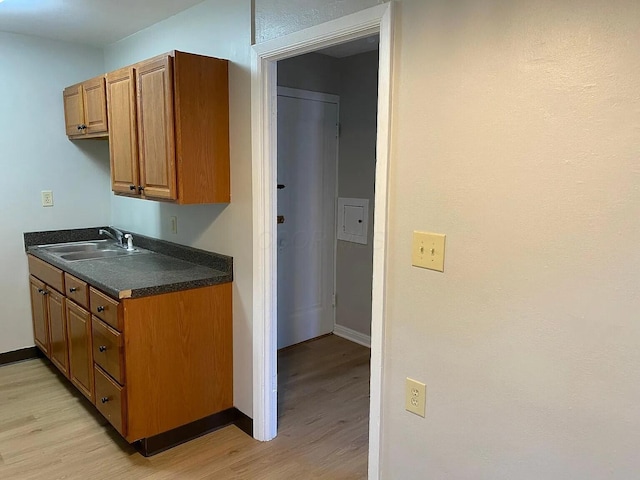 kitchen featuring light wood-style flooring, a sink, baseboards, brown cabinetry, and dark countertops