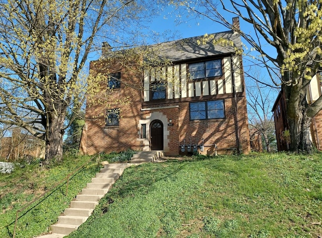 tudor-style house with a chimney, a front lawn, and brick siding