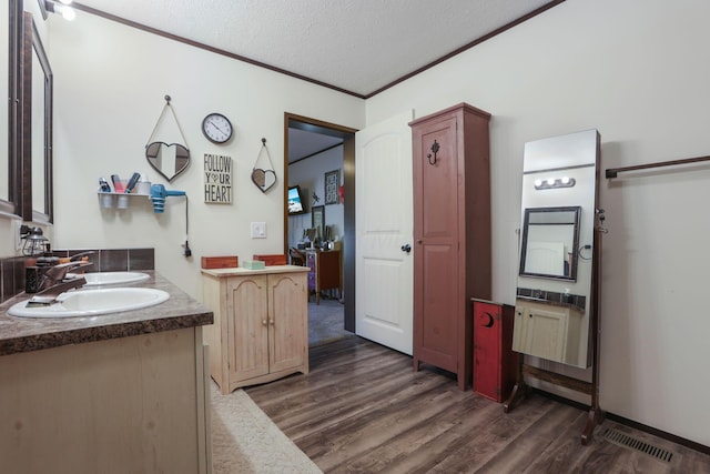 bathroom featuring a textured ceiling, wood finished floors, visible vents, vanity, and ornamental molding