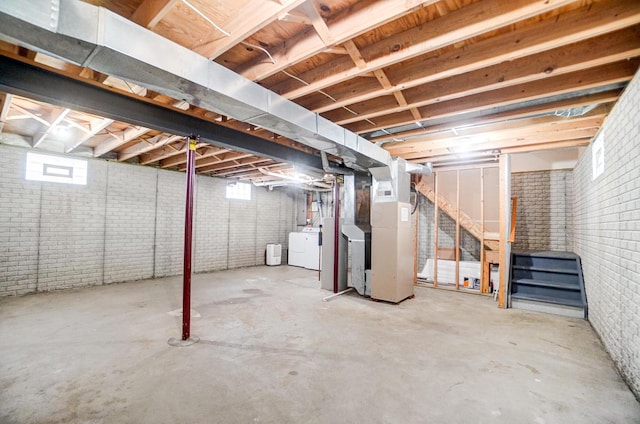 below grade area featuring heating unit, brick wall, and separate washer and dryer