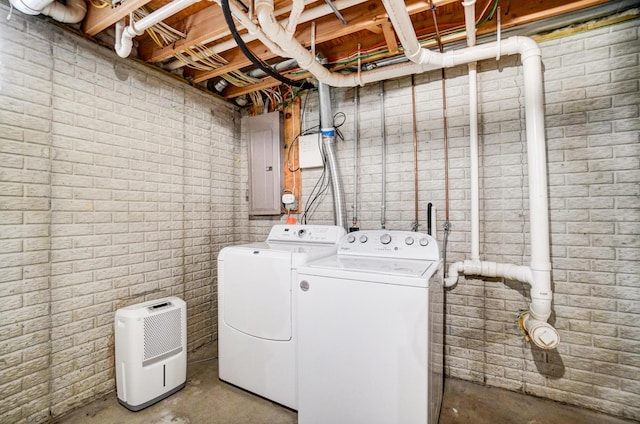 laundry room featuring laundry area, electric panel, separate washer and dryer, and brick wall