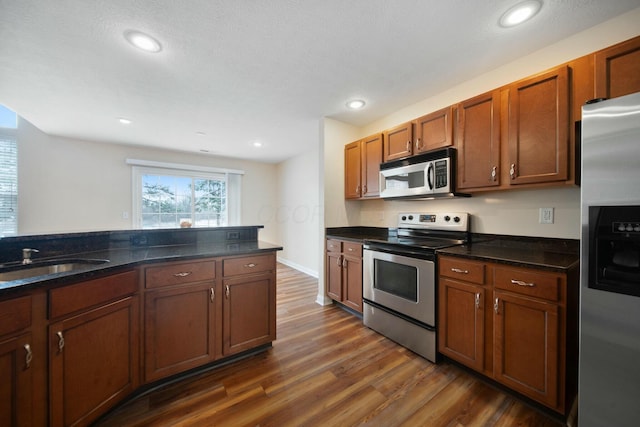 kitchen with recessed lighting, dark wood-type flooring, a sink, appliances with stainless steel finishes, and brown cabinetry