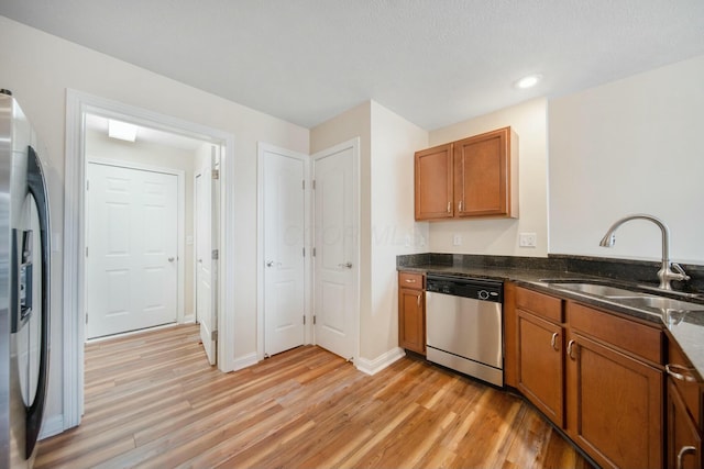 kitchen featuring stainless steel appliances, a sink, light wood-style flooring, and brown cabinets