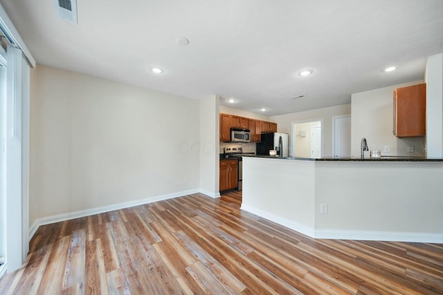 kitchen featuring visible vents, light wood-style floors, appliances with stainless steel finishes, brown cabinets, and dark countertops