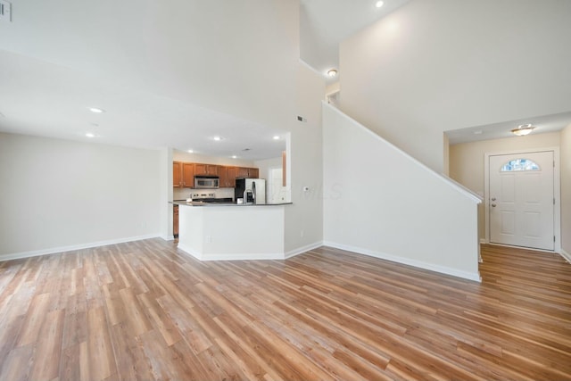 unfurnished living room featuring light wood-style floors, recessed lighting, a high ceiling, and baseboards