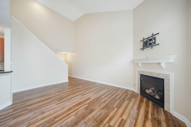 unfurnished living room featuring high vaulted ceiling, a tiled fireplace, wood finished floors, and baseboards