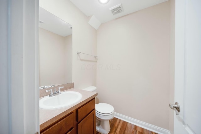 half bath featuring toilet, wood finished floors, visible vents, vanity, and baseboards