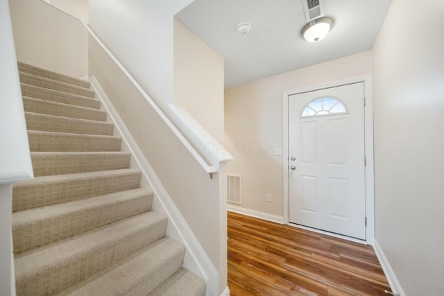 foyer entrance with stairway, baseboards, visible vents, and wood finished floors