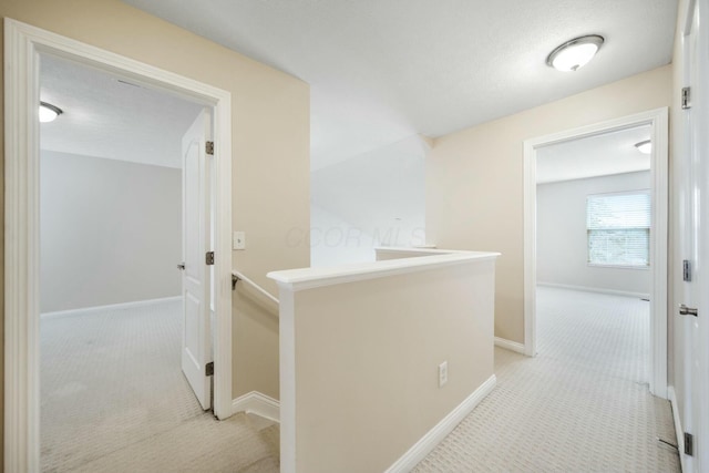 corridor featuring baseboards, light carpet, and an upstairs landing