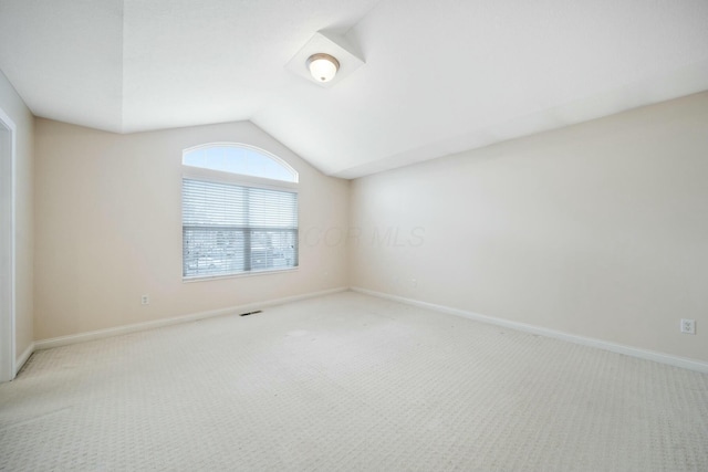 carpeted empty room featuring visible vents, vaulted ceiling, and baseboards