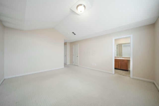 unfurnished bedroom with light colored carpet, vaulted ceiling, baseboards, and ensuite bathroom