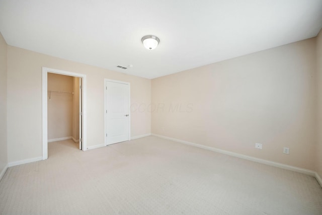 unfurnished bedroom featuring light colored carpet, visible vents, baseboards, a closet, and a walk in closet