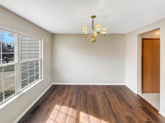 unfurnished room with a chandelier, plenty of natural light, wood finished floors, and baseboards