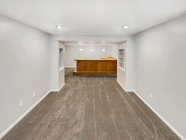 unfurnished living room with a bar, carpet, built in shelves, and baseboards