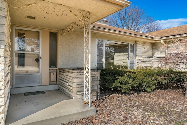 view of exterior entry with stone siding, visible vents, and stucco siding