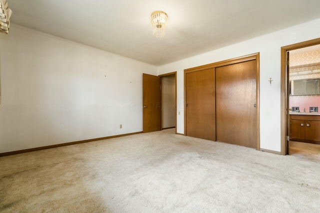 unfurnished bedroom with a closet, baseboards, light colored carpet, and ensuite bath