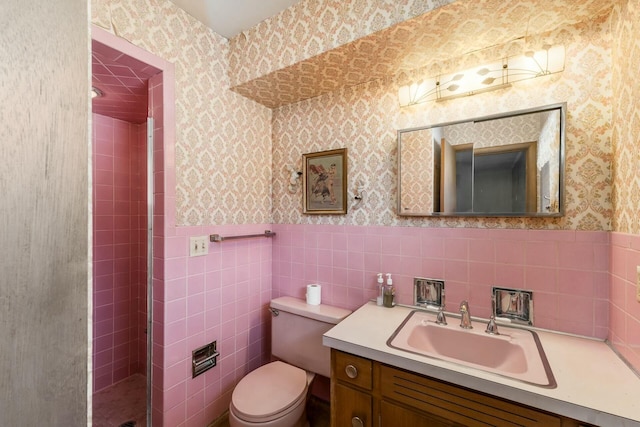 bathroom featuring toilet, a wainscoted wall, tile walls, vanity, and wallpapered walls