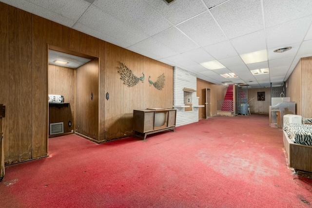 interior space featuring a paneled ceiling, carpet, visible vents, and wooden walls