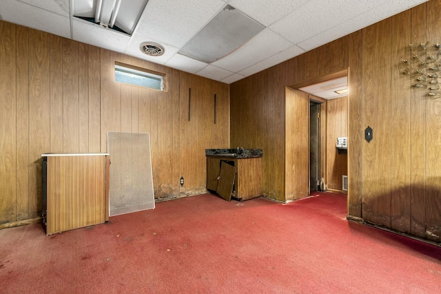 interior space featuring wood walls, a drop ceiling, carpet flooring, and visible vents