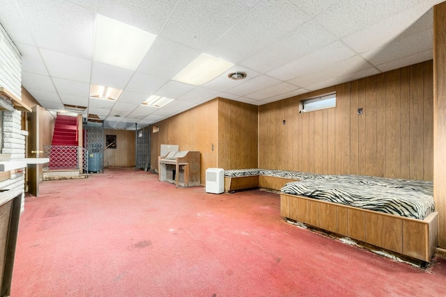 finished basement featuring carpet floors, wood walls, stairway, and a drop ceiling