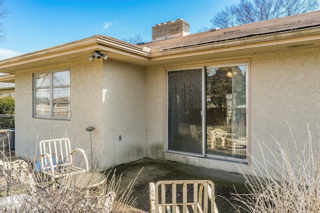 back of house with a chimney and stucco siding