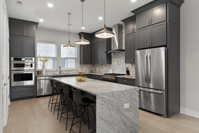 kitchen featuring backsplash, wall chimney range hood, light stone countertops, stainless steel appliances, and a sink