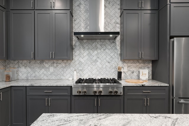 kitchen featuring light stone counters, tasteful backsplash, appliances with stainless steel finishes, and wall chimney exhaust hood