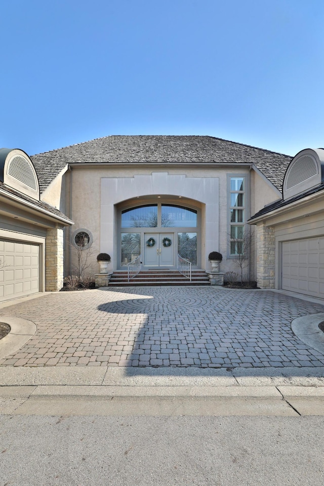 view of front facade with stone siding, french doors, decorative driveway, and a garage