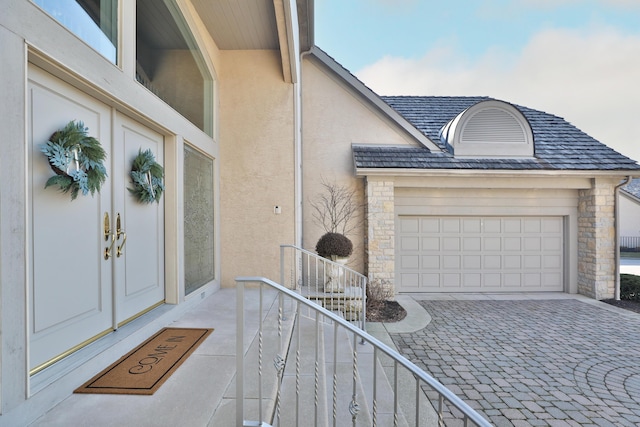 view of exterior entry featuring stone siding, stucco siding, an attached garage, and decorative driveway