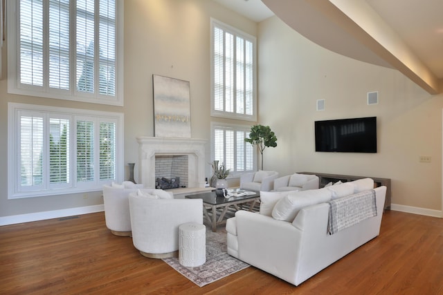 living area with visible vents, wood finished floors, a high end fireplace, baseboards, and a towering ceiling