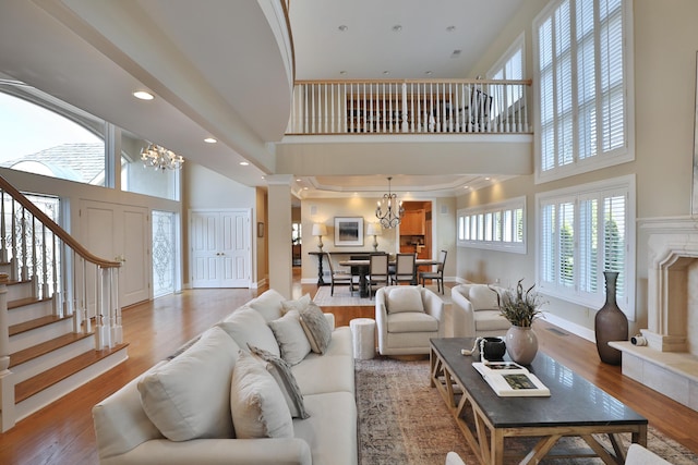 living area with a high ceiling, stairs, an inviting chandelier, and wood finished floors