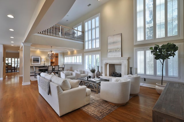 living area featuring wood finished floors, baseboards, a high ceiling, decorative columns, and a fireplace with raised hearth