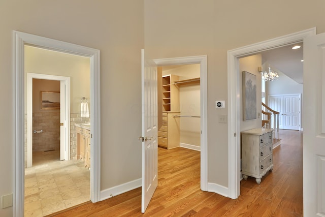 corridor featuring an inviting chandelier, baseboards, and light wood finished floors