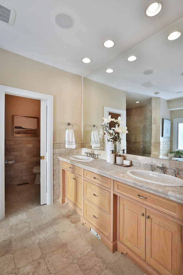 bathroom with visible vents, a sink, recessed lighting, tile walls, and double vanity