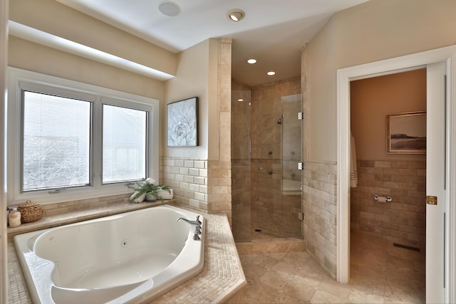 bathroom featuring tile walls, a tub with jets, a stall shower, and tile patterned flooring