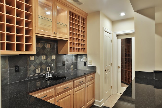 kitchen featuring dark stone countertops, light brown cabinets, visible vents, a sink, and decorative backsplash