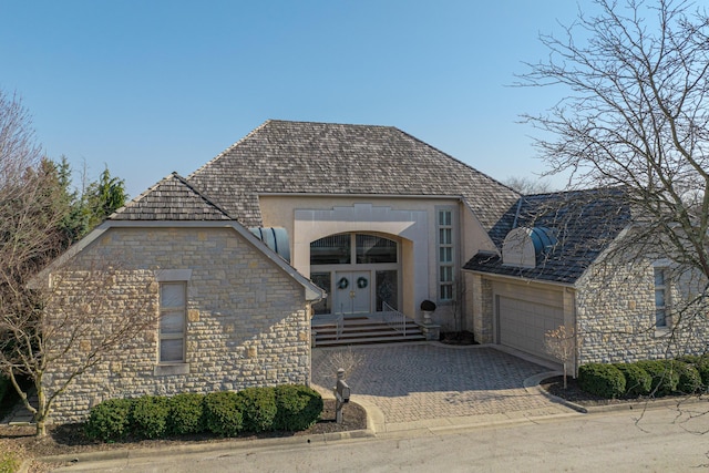 french country home featuring stone siding, decorative driveway, and a garage